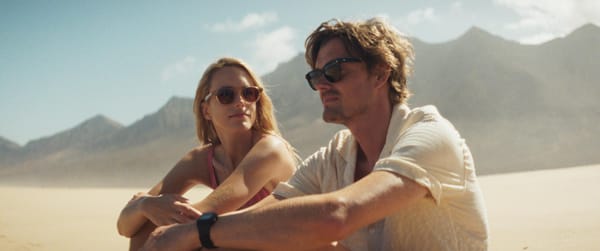 A still from the film Islands, showing Sam Riley and Stacy Martin sitting on a beach